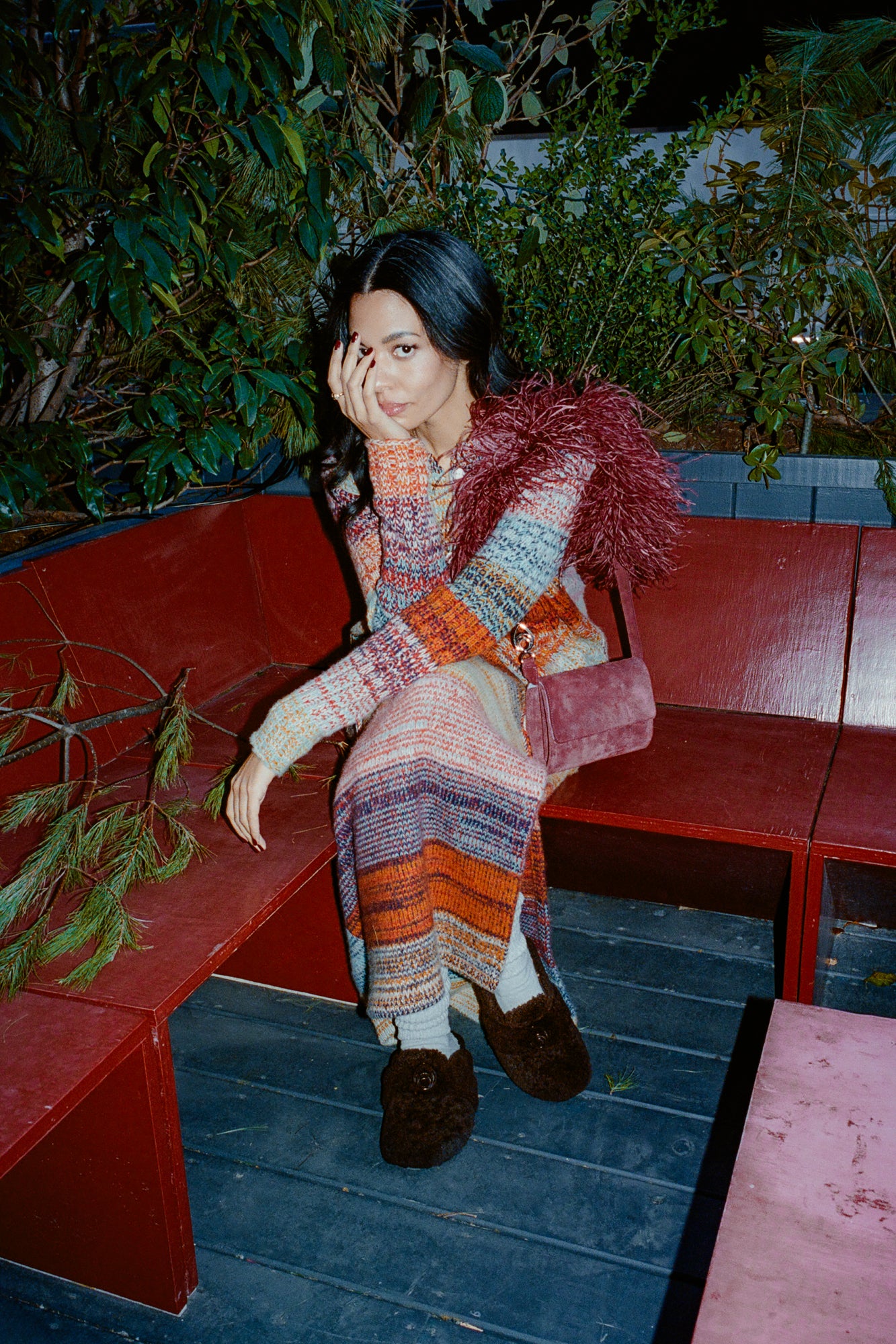 Woman wearing shearling mules and a long striped sweater dress, sitting on a bench.