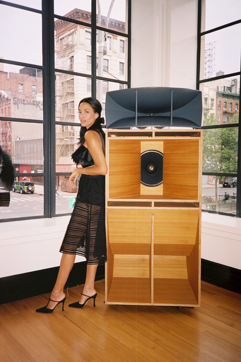 Brother Vellies Founder Aurora James in Olivia Pumps in Midnight Nylon leaning against a mid century style sound system