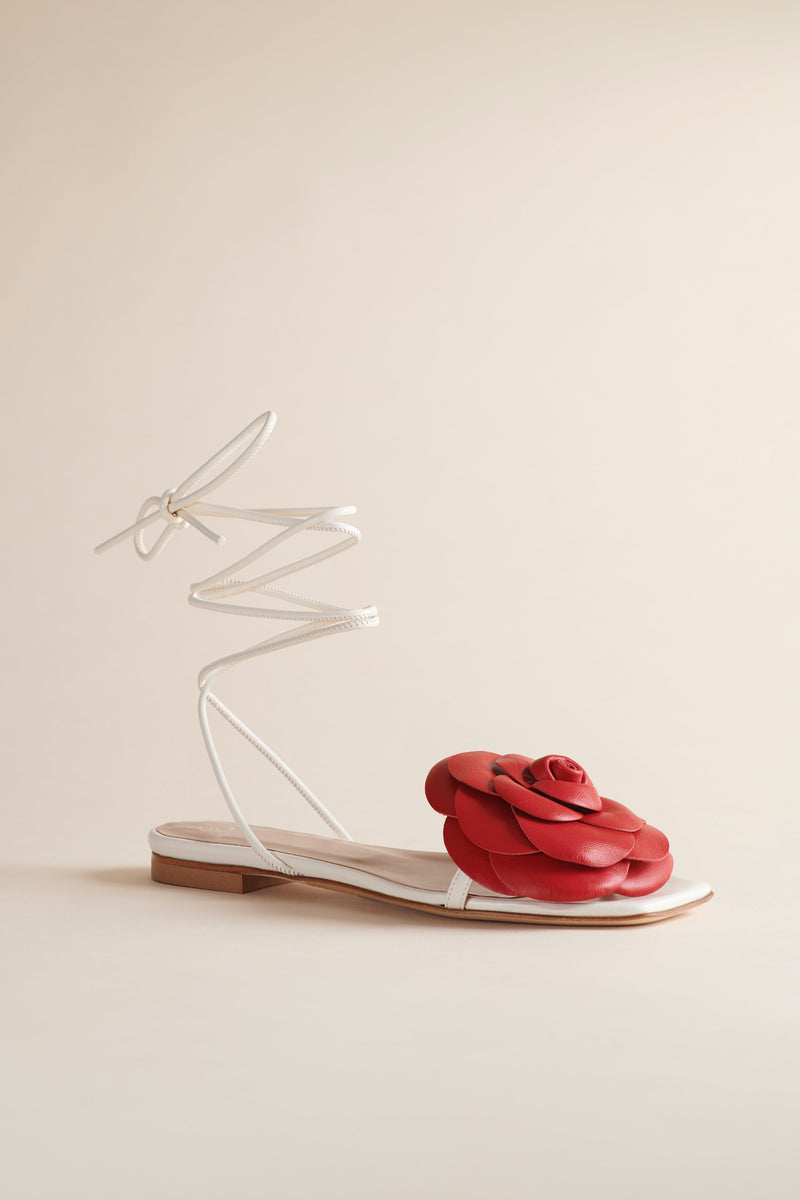 Brother Vellies LIlia Flat Sandal in Ivory with red rose on the foot and ivory patent leather laces, angled, on a beige backdrop