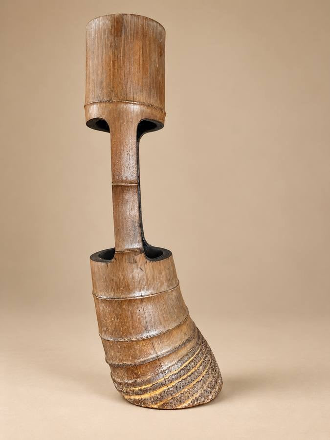 A sculptural wooden bamboo Ikebana vase with a cylindrical top, hollow center channel, and a wide, ribbed lower base, shown on a plain beige studio background.