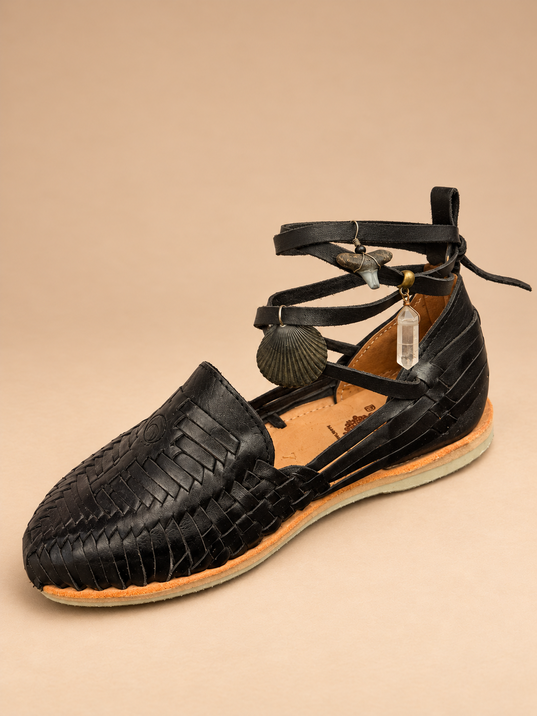 Candy Huaraches 013 in black woven leather, three-quarter view with ankle laces and shell, shark tooth and quartz charms.