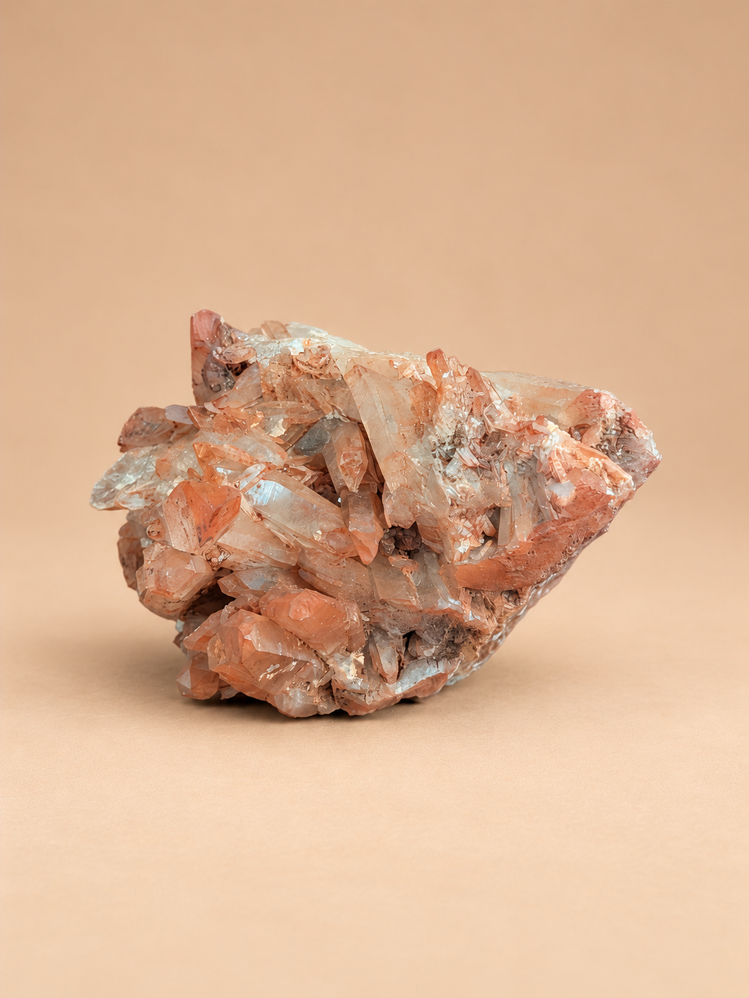 A rough mineral or crystal cluster with translucent pale blue and orange-red crystalline formations, photographed on a smooth warm beige background.