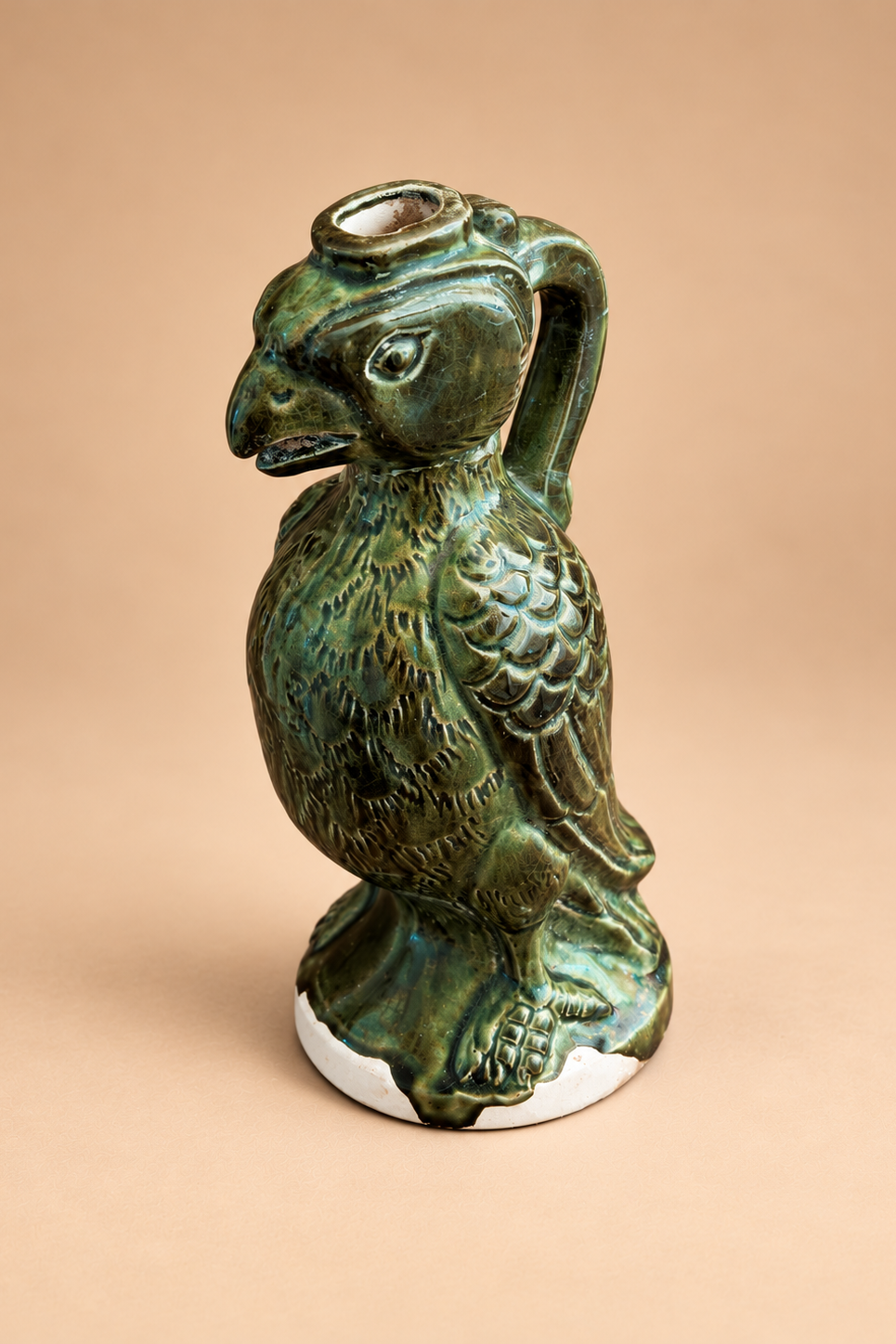A green glazed ceramic bird-shaped vessel with a handle and small top opening, photographed against a plain warm beige background.