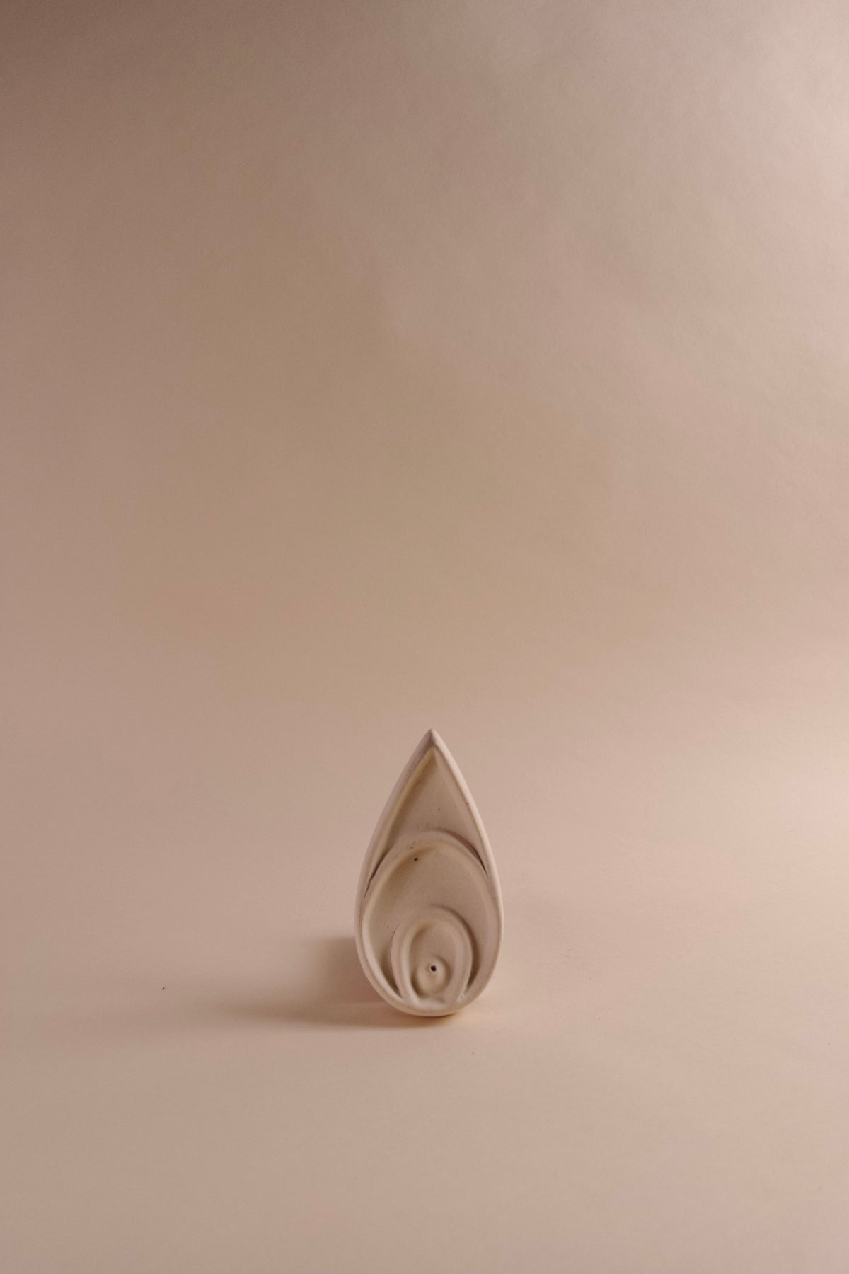 A white incense dish with a floral design, placed on a beige background.