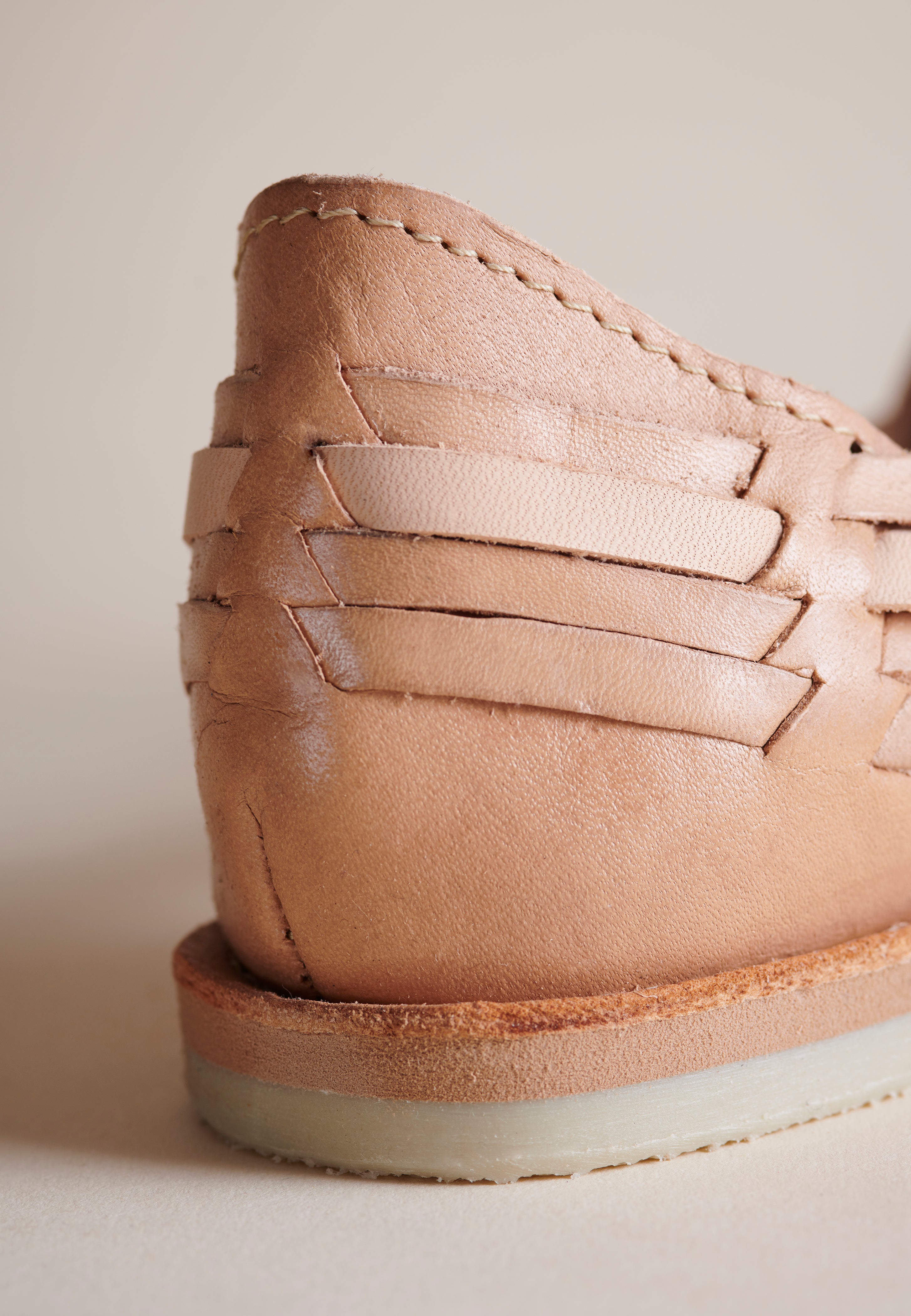 Close-up of the rear heel and side strap detailing of a light tan leather shoe on a neutral beige background.