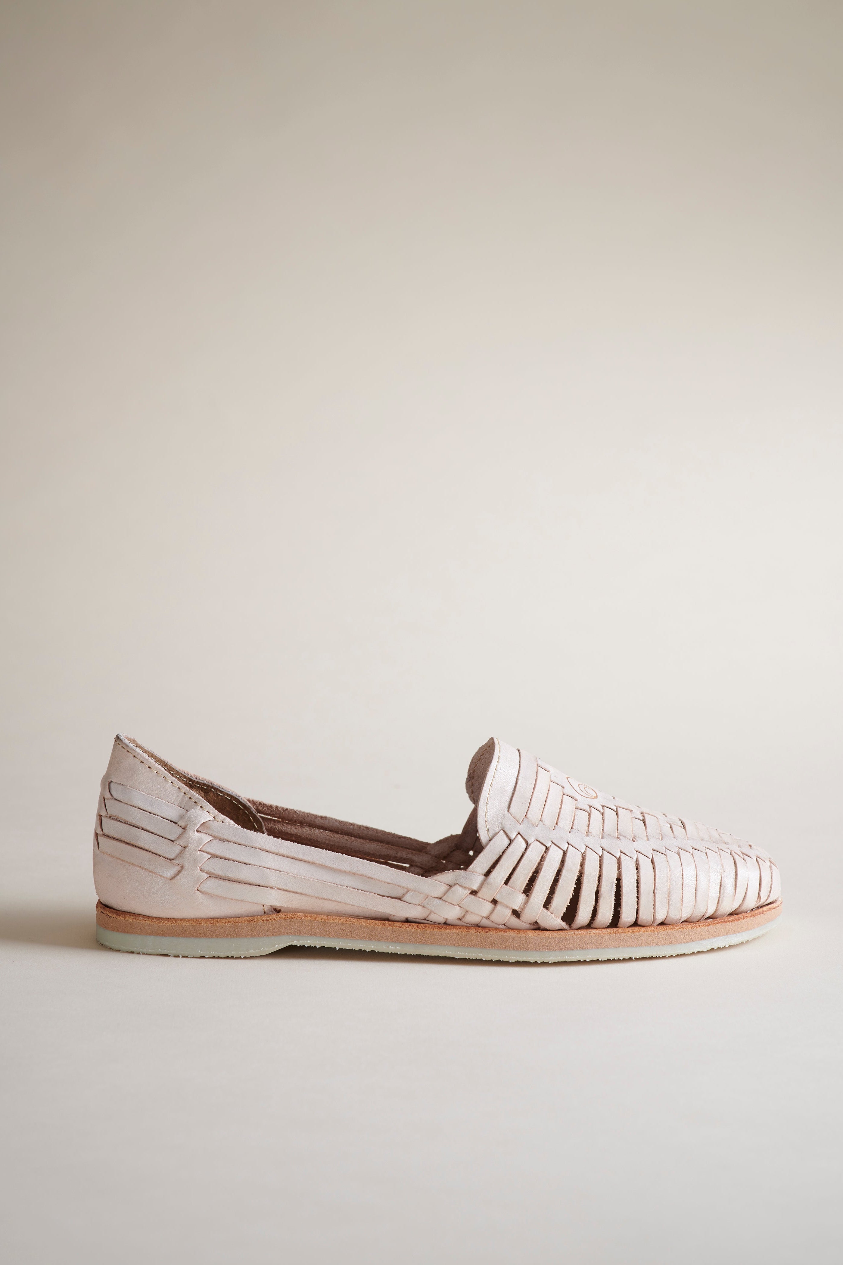 A single woven leather loafer in a pale blush pink color, shown in profile against a neutral beige background.