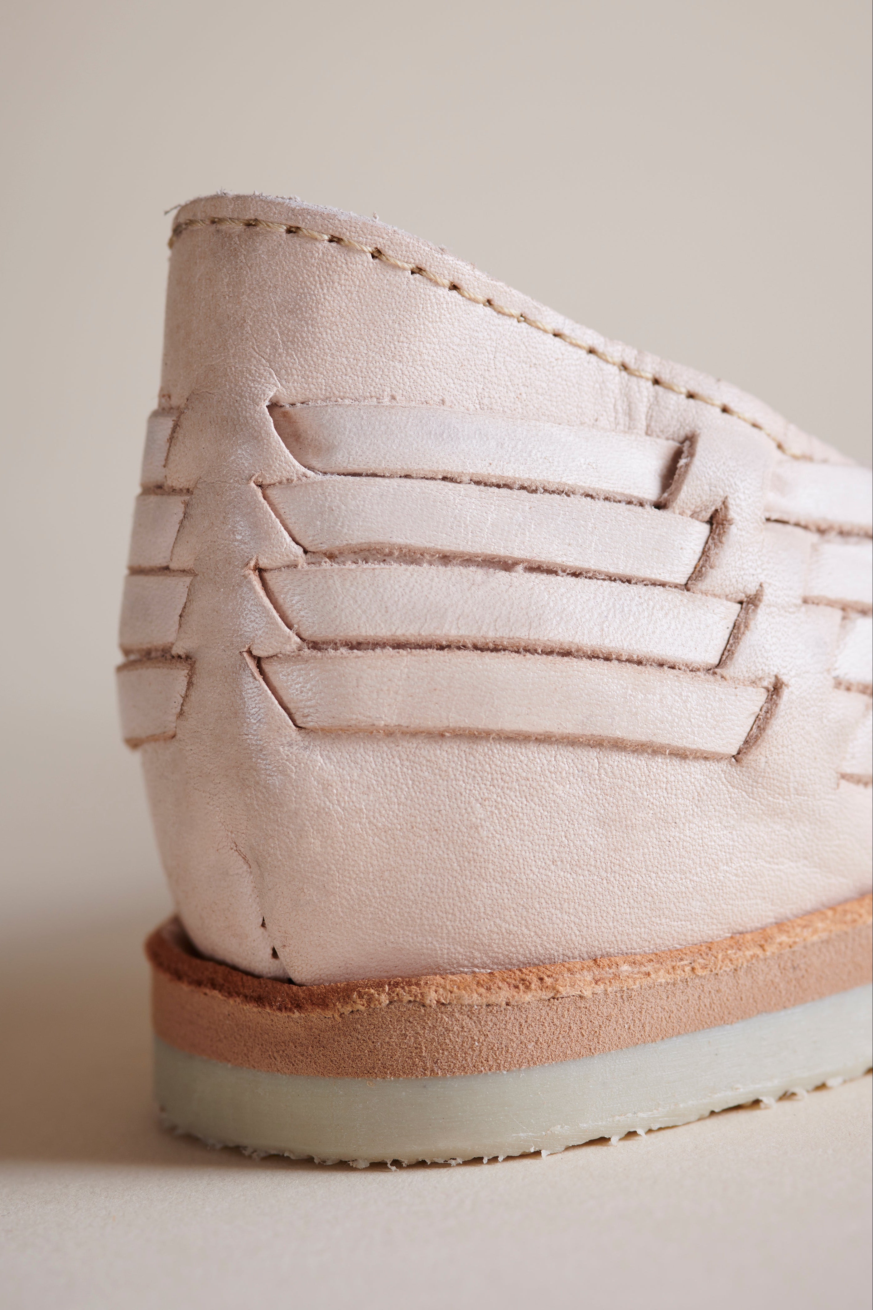 A close-up shot of a light beige leather shoe showing the side profile, featuring decorative horizontal strap details and a layered sole.