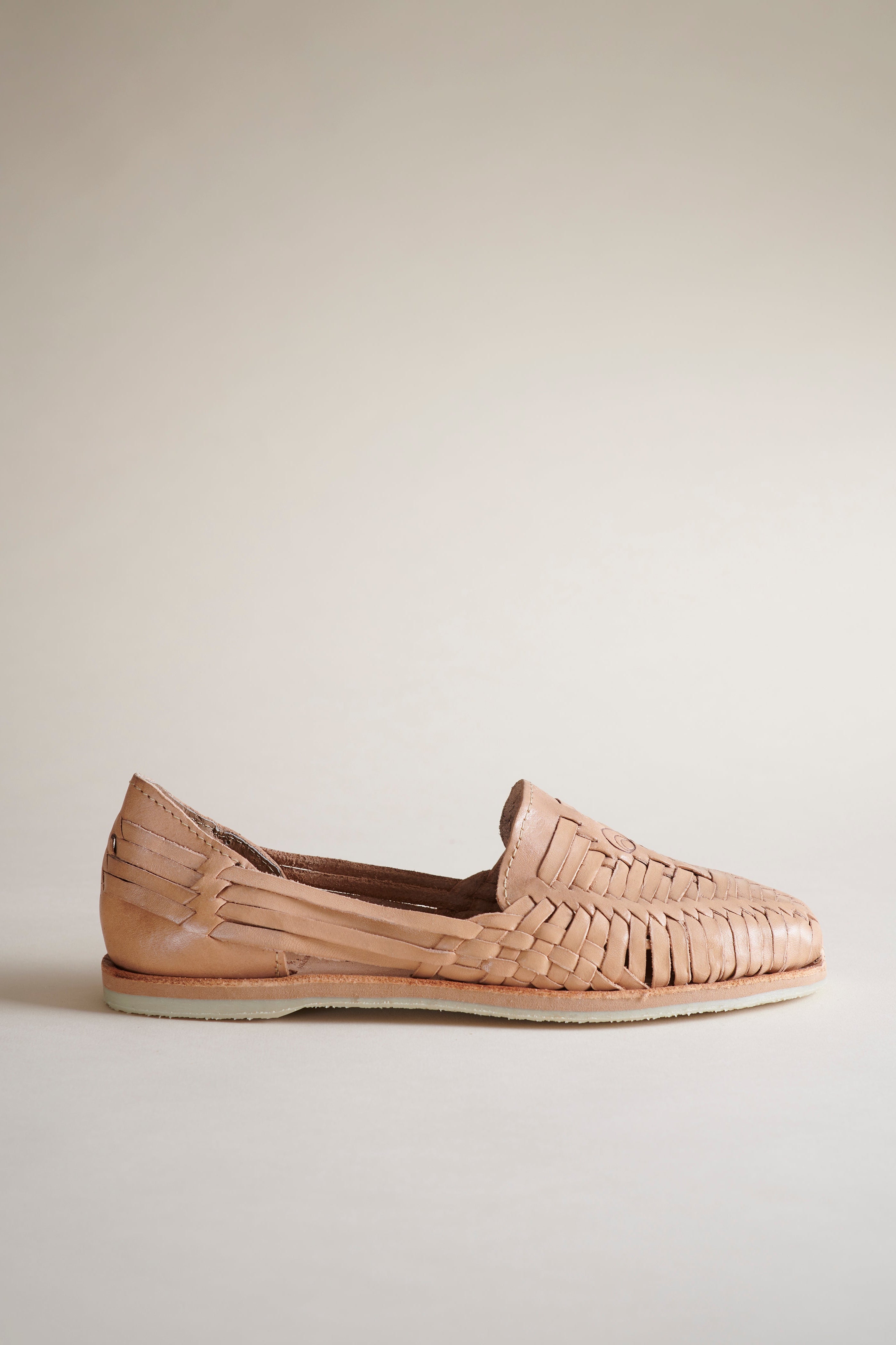 A single woven leather loafer in a light tan or blush-beige color, shown in profile against a neutral, warm off-white background.