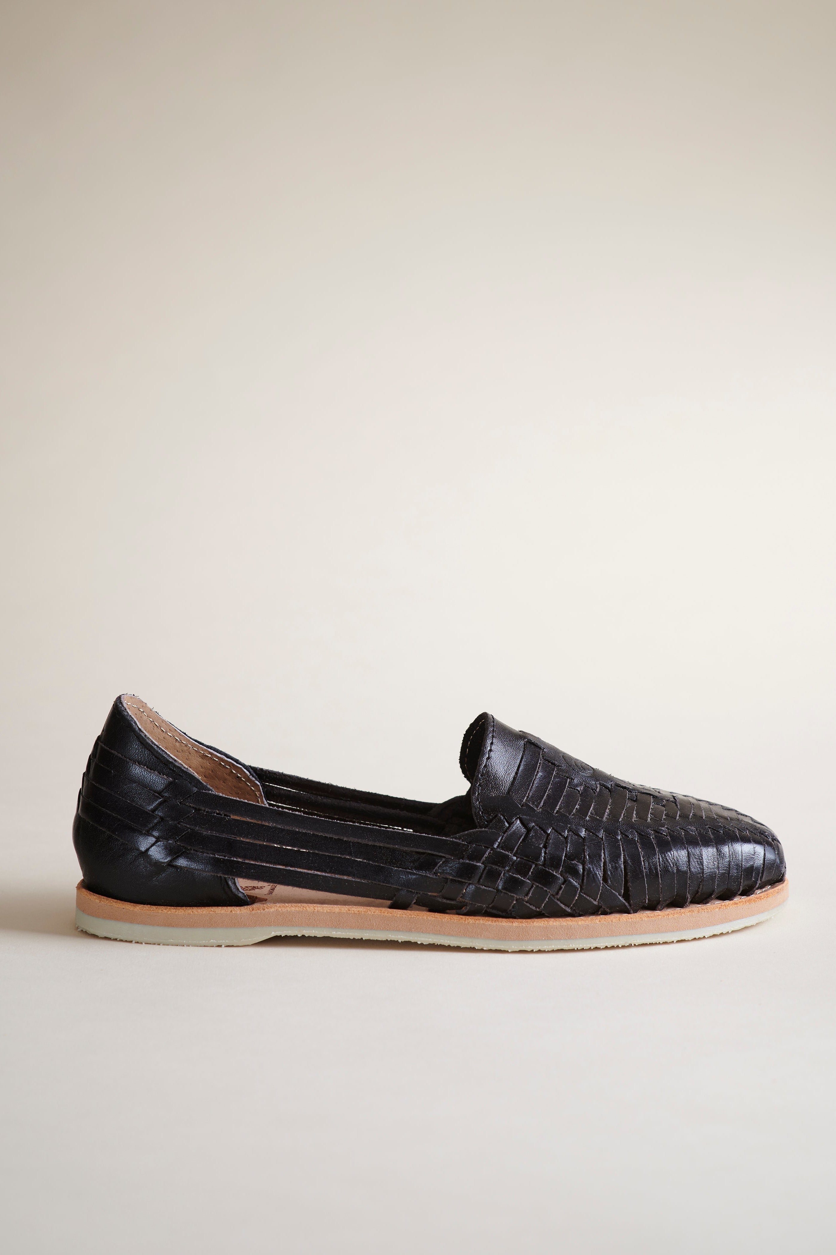 Black braided leather shoe with a tan sole on a white background