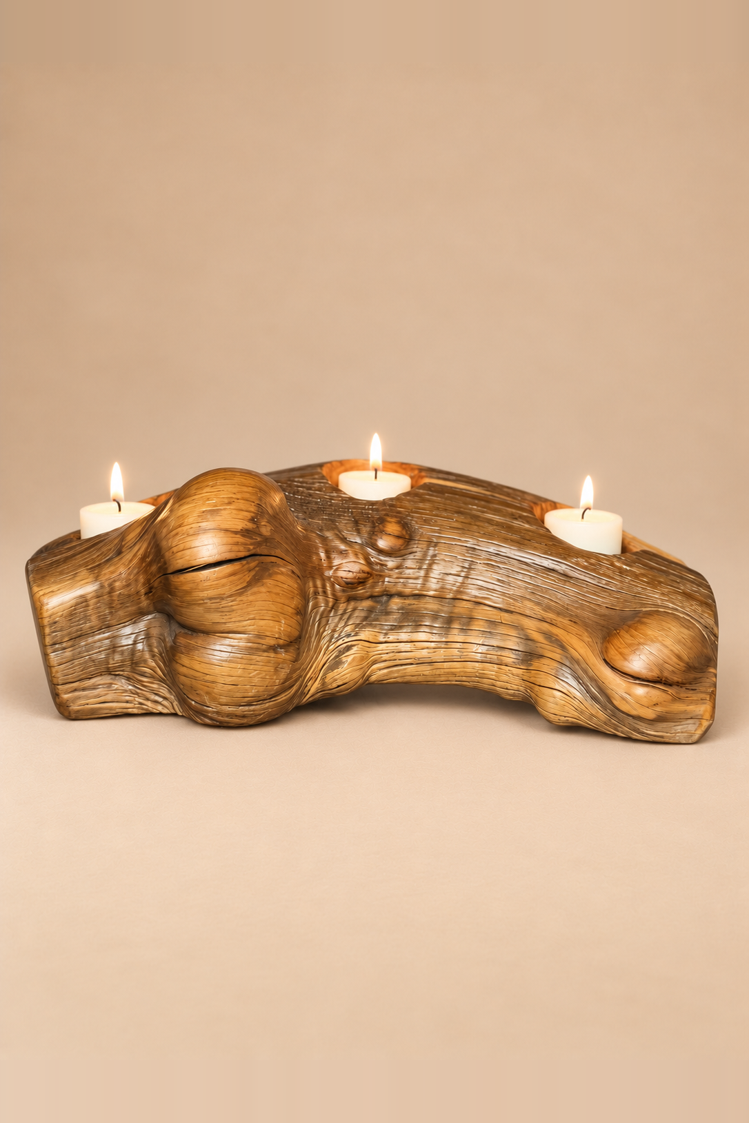 A mid-century modern carved teak wooden candle holder shaped like a tree trunk, holding three lit white pillar candles, set against a solid beige background. Burled wood with natural striations