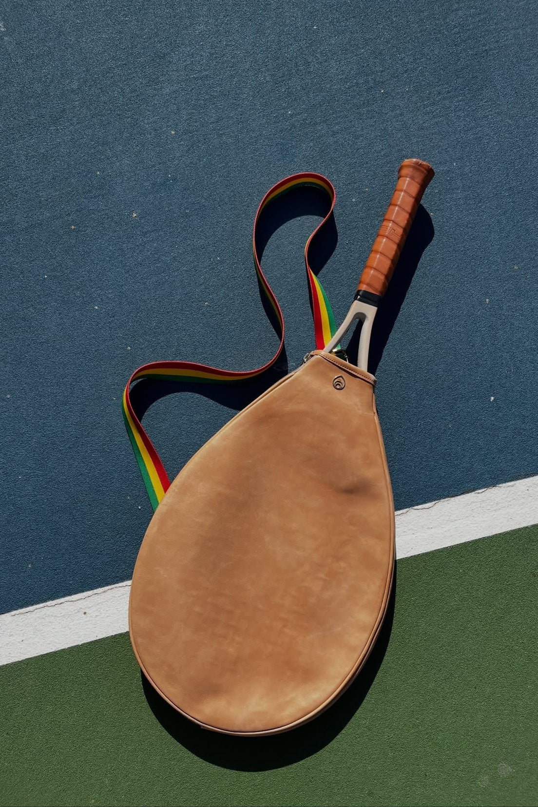 aerial view of a tennis racquet in a leather sleeve laid on a tennis court